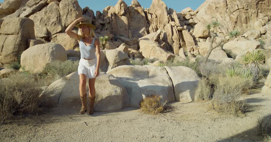 A woman sitting on a large rock in the desert stands up and walks away