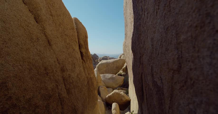 The video shows a firstperson perspective of a person walking through a narrow rock formation in a desert the rock walls are light brown and textured with smaller rocks scattered on the ground