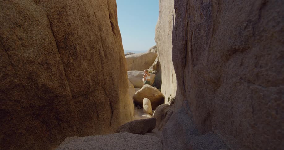 Woman standing on rocks is seen through a narrow passage between cliffs