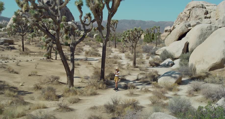A woman walks through a desert on a path surrounded by large rocks
