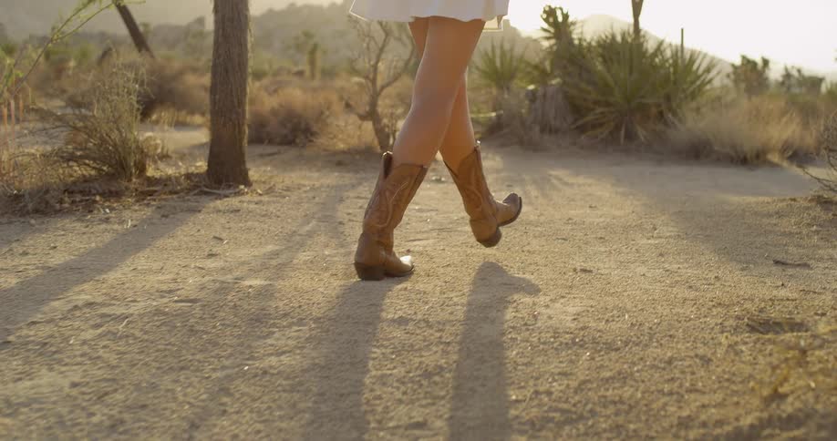 The woman is hiking past the shrubs and sand