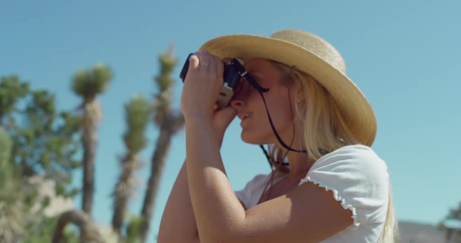 A young woman in the jungle taking photos of her surroundings with a digital camera under the sun wearing a sun hat