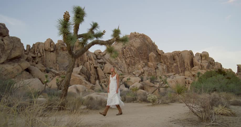 Woman in white dress walks on desert trail surrounded by rocks