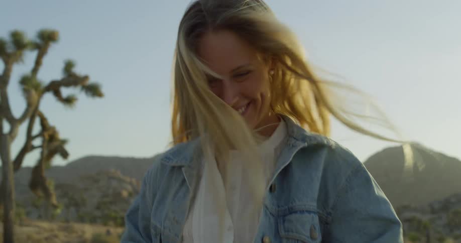A smiling woman runs joyfully through a desert landscape at sunset