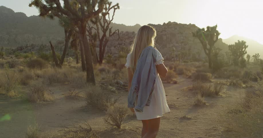 Woman walks along a desert trail during sunset