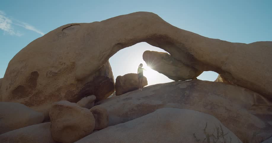 Lone figure stands beneath a natural rock arch in the desert