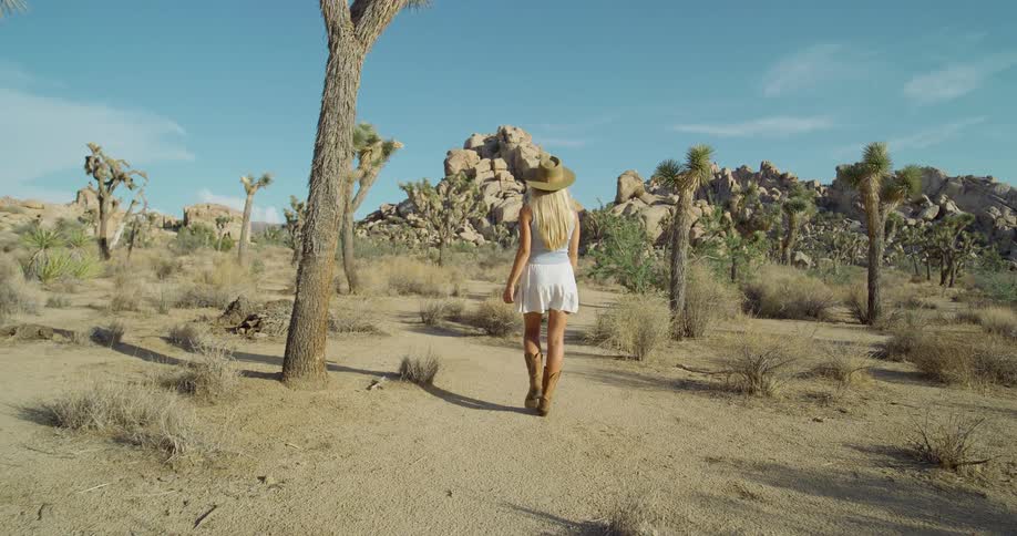 The woman is hiking past trees in the desert