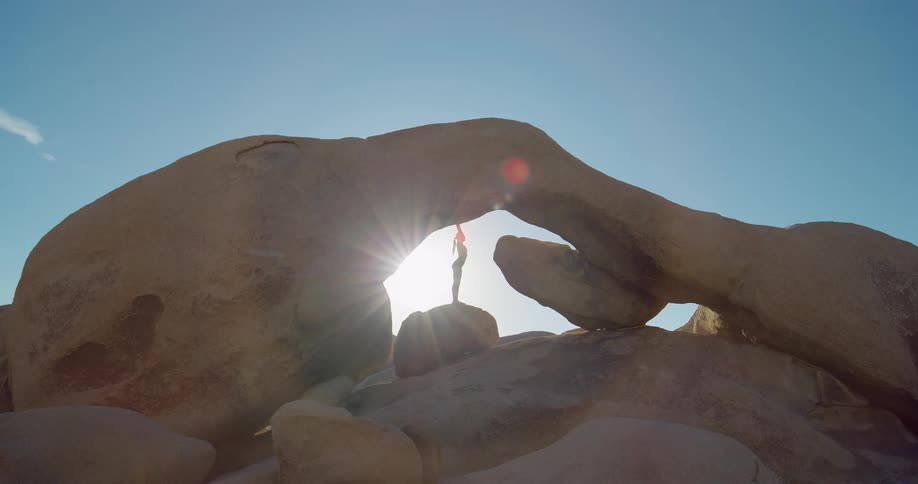 A woman doing yoga on top of a rock arch mountain at midday