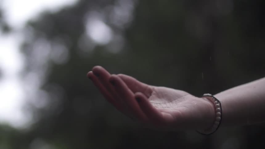 A woman holding her hand out, with her palm towards the sky, to catch raindrops