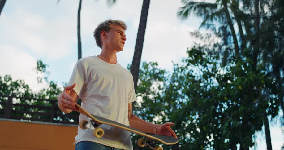 Young man spinning skateboard with his hands in an outdoor area surrounded by palm trees