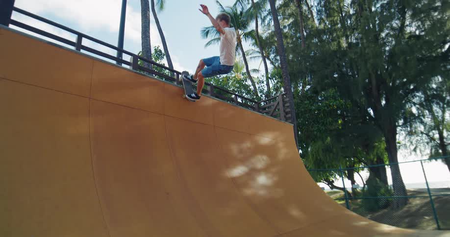 A young man skateboards up a tall ramp on a partly sunny summer day