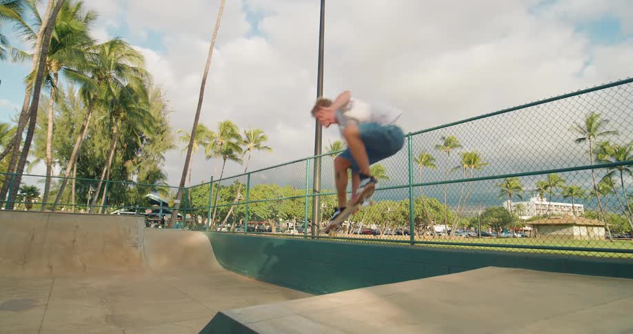 A young man in a skateboard park riding a skateboard and performing stunts at midday