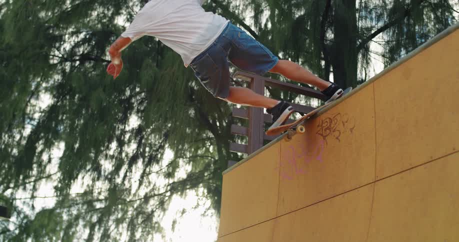 A young man is seen skateboarding on a yellow halfpipe performing a trick on the edge of the ramp