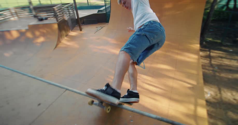 A skateboarder in a white shirt and denim shorts rides on a wooden ramp in a park