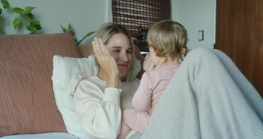 Smiling mother interacts with her young daughter sitting on her lap on the couch