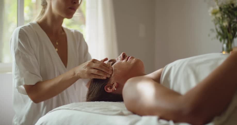 Woman lying down receives a relaxing facial massage in a bright room
