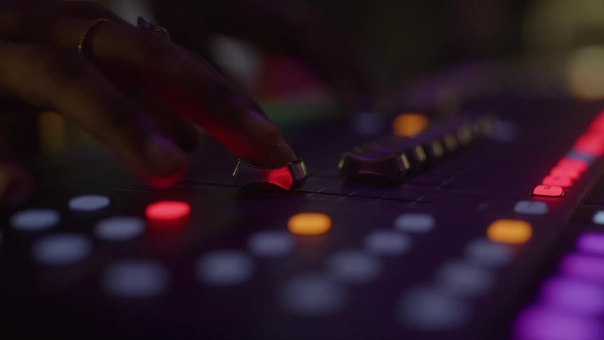 Hand adjusts illuminated controls on a sound mixer