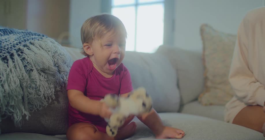 Little girl holds a stuffed toy while mother smiles beside her on the couch
