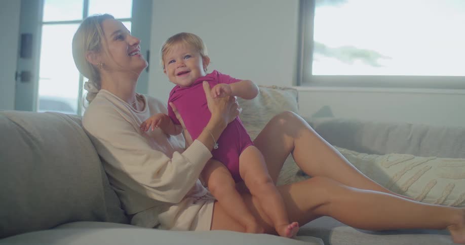 Mother plays with a smiling baby on the couch