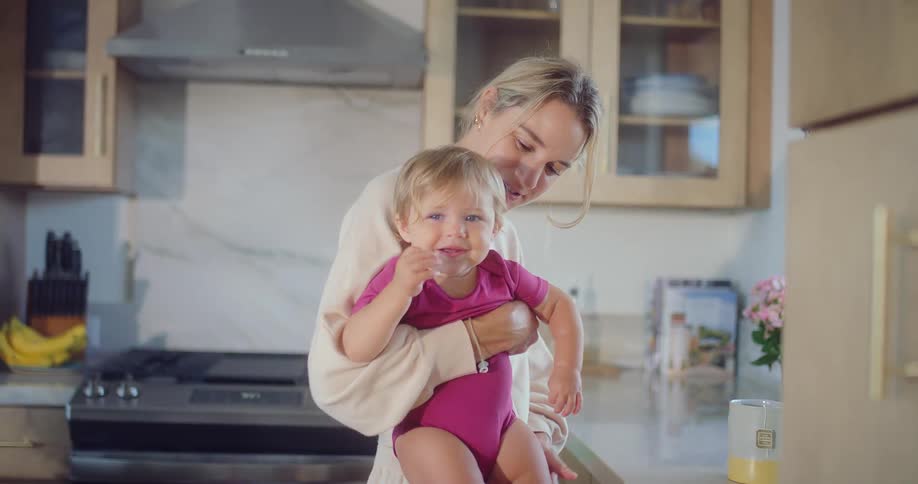 The mother smiles while holding her daughter in the kitchen