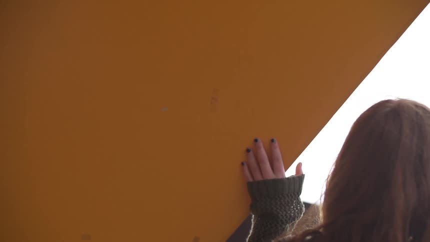 Woman walks around corner holding wall