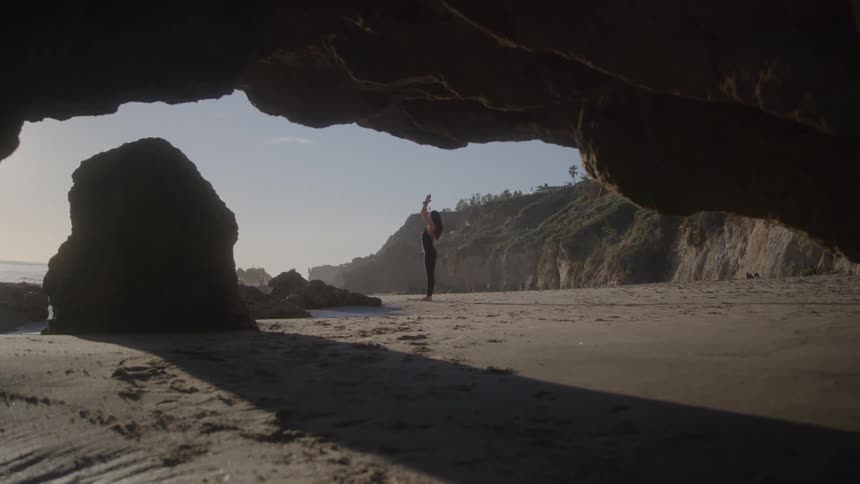 Person practicing yoga on a beach surrounded by rocky cliffs