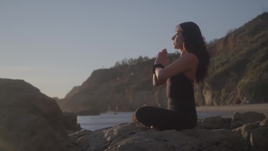 The woman is meditating on the rocks