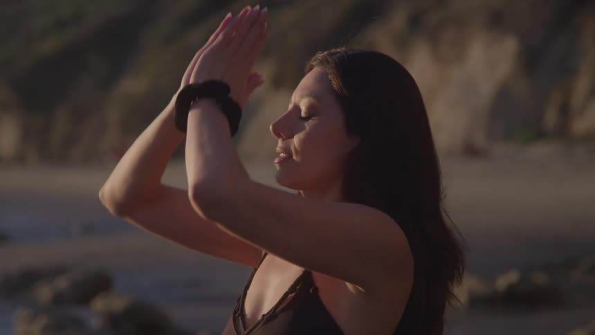 A darkhaired woman practices yoga outdoors while at the beach