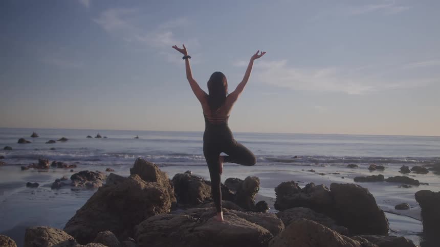 Woman practices yoga pose in balance on rocks by the sea