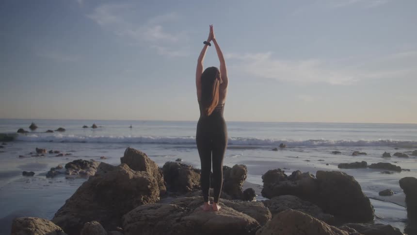 The woman is doing yoga on the rocks
