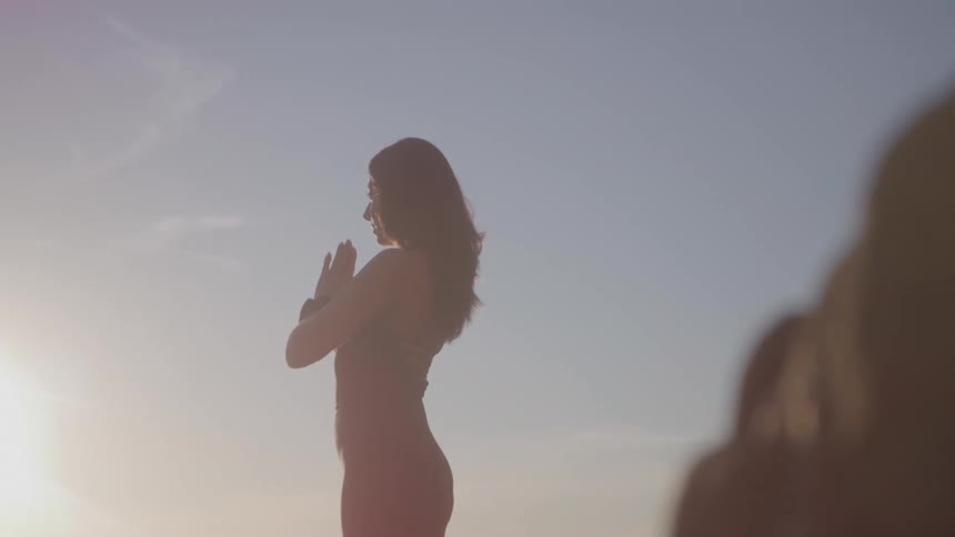 Woman practicing yoga in prayer position on the beach at sunset