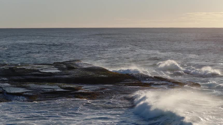 Waves crashing against a rock in the middle of the ocean at midday
