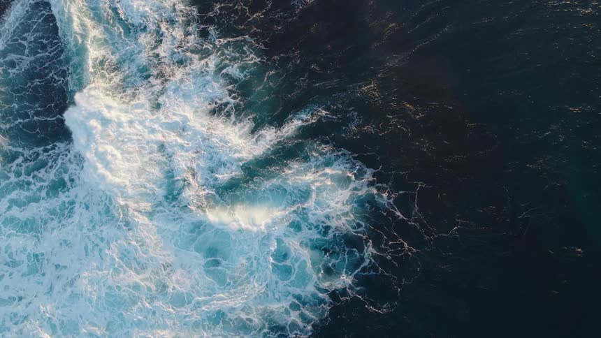 Aerial view of ocean waves crashing and swirling in deep blue water