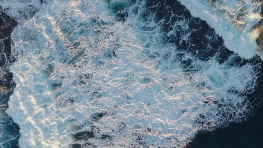Aerial view looking down at waves splashing and rolling into shore