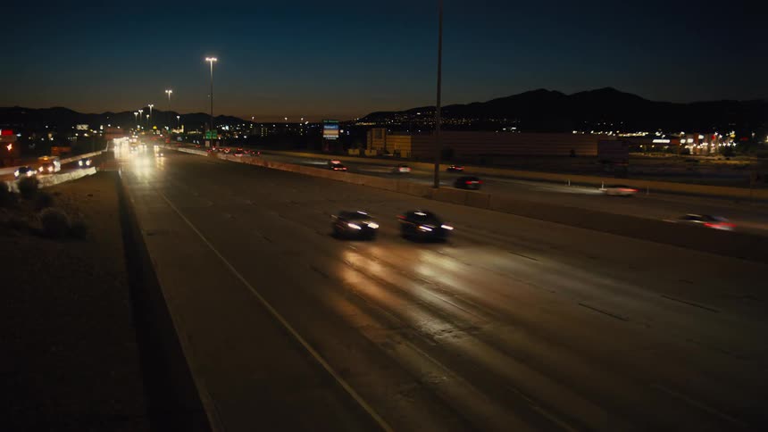 Cars move along a busy highway at dusk with city lights glowing behind