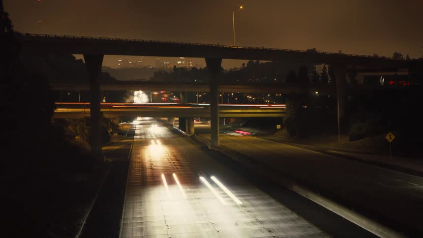 A timelapse video shows a highway intersection at night the headlights and taillights of the cars create long streaks of light as they pass