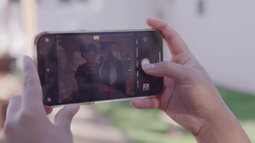 Close up of a girl using a mobile phone to take graduation photos outdoors during daytime