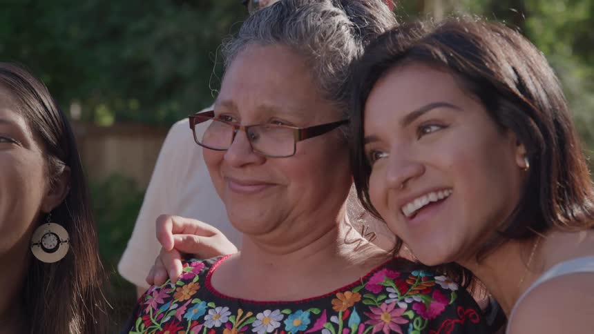 Older woman with glasses is embraced by smiling young woman outdoors