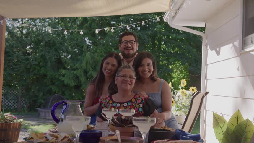 A family smiles together at an outdoor table with food and drinks