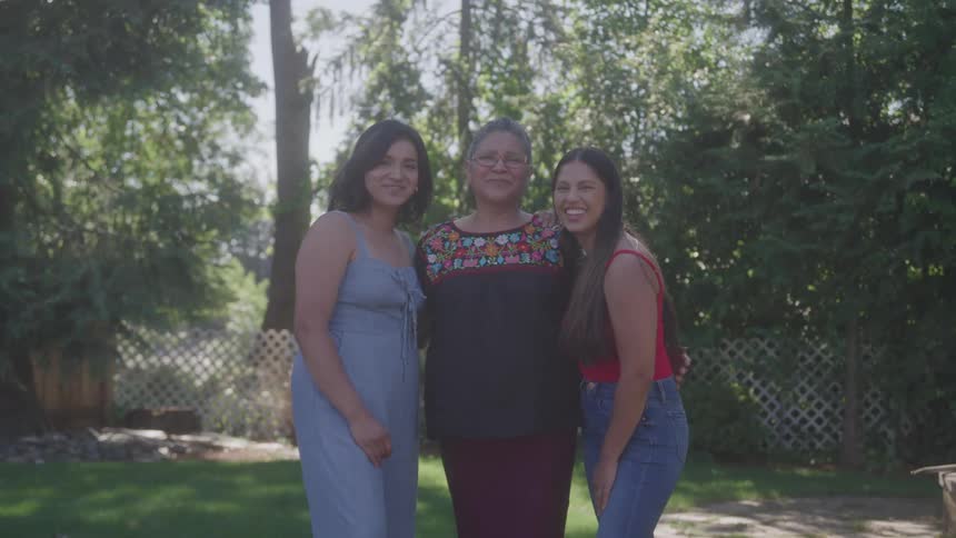 Three women pose smiling side by side in a sunny garden