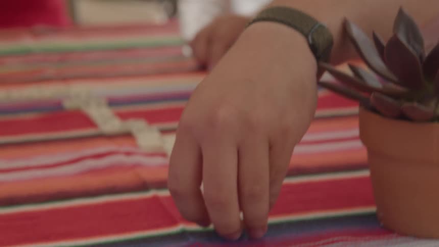 A man places a domino tile on a striped tablecloth
