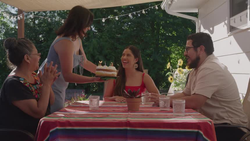 Three people talk and laugh around a colorful table outdoors