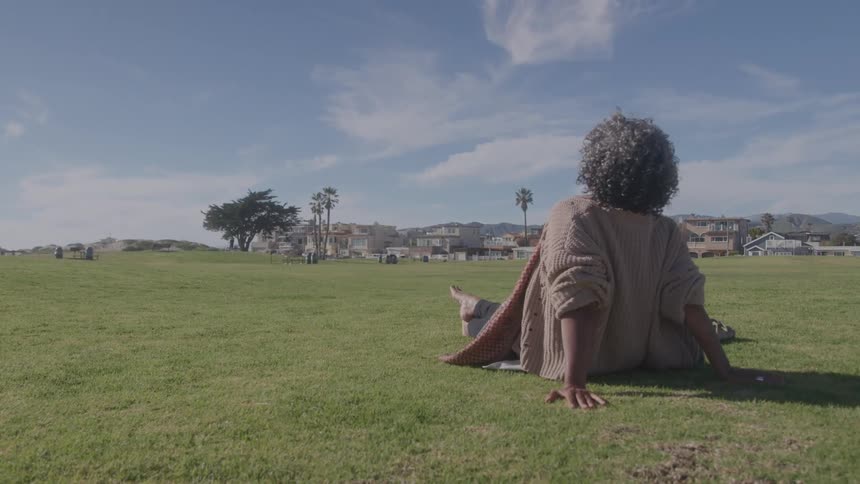 A person relaxes on the grass overlooking houses and palm trees