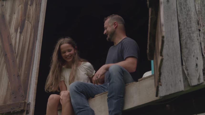 Man sitting on wooden ledge hugs smiling girl by his side
