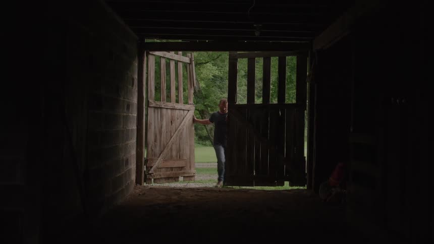 Man closes barn doors overlooking outdoor green area