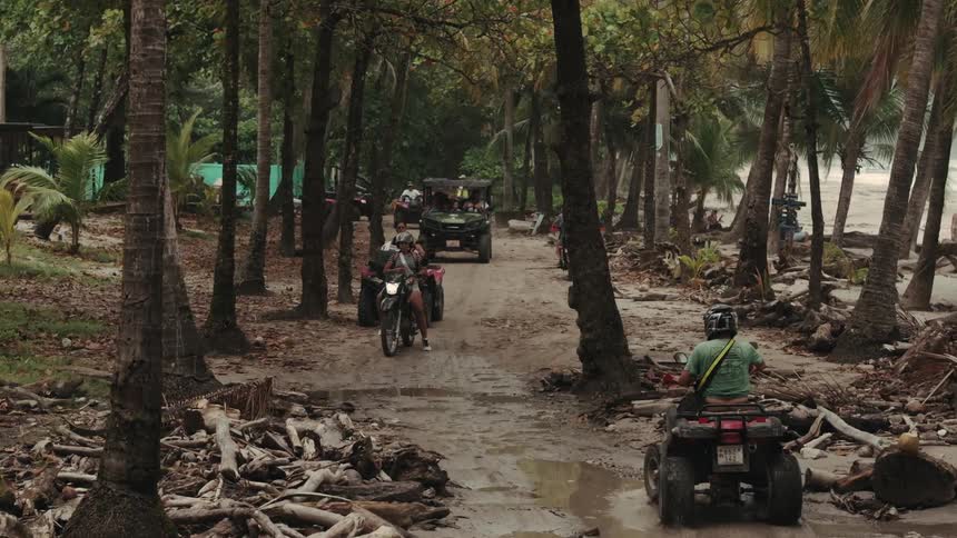 A group of people driving their vehicles along a rough road lined with trees on each side