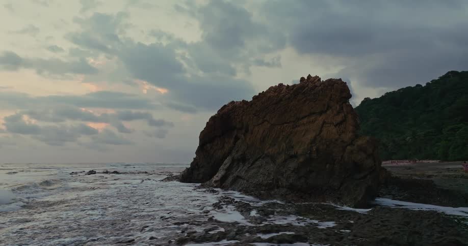 Rock formation by the sea with waves breaking at sunset