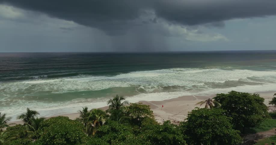 A tropical island beach on a dark cloudy day with heavy waves crashing against the shoreline