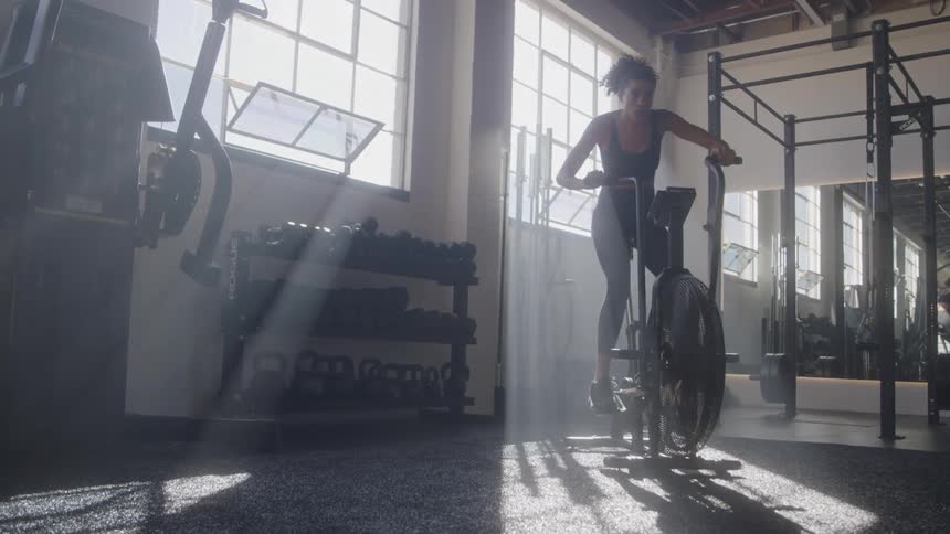 Woman works out on a stationary bike under a beam of natural light