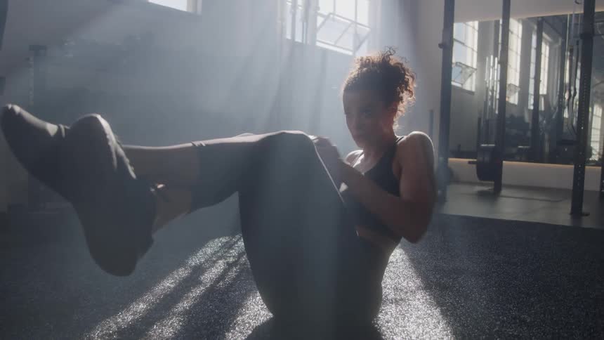 A woman doing focused core work with a medicine ball in dramatic light